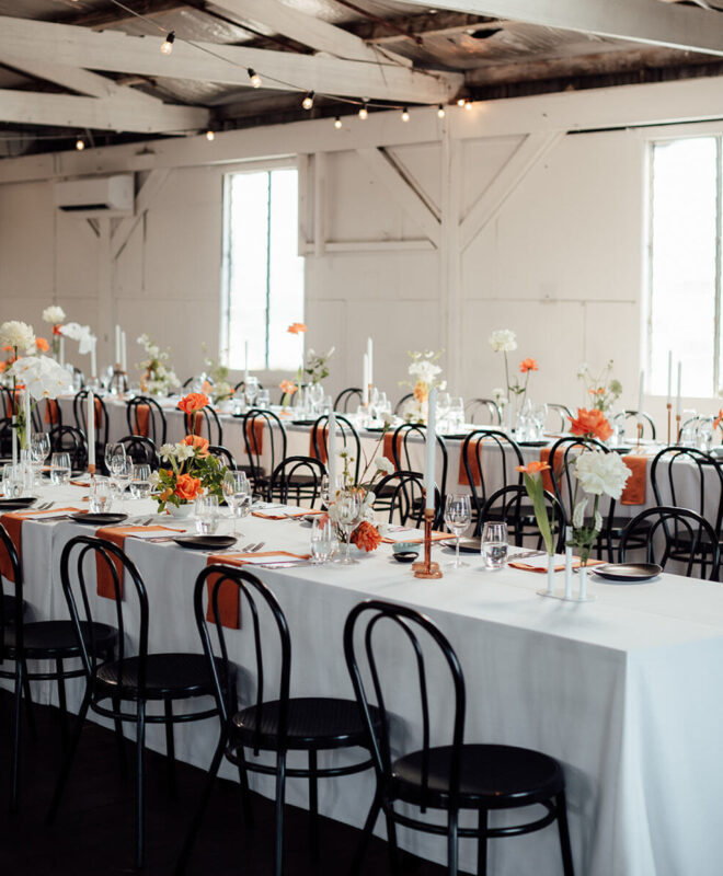Beautiful wedding reception at Gather and Tailor, featuring exquisite styling by The Goodsmiths, vibrant orange and white floral arrangements by Anatomy of Flowers, and elegant candles.