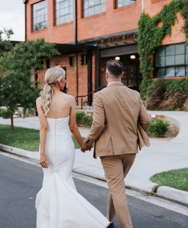 A happily married couple walks hand in hand outside The Button Factory, a unique and historic Melbourne wedding venue, celebrating their new beginning in front of this stylish event space.