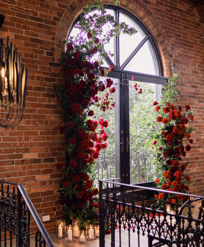 The iconic Chapel 1885 arch window, beautifully framed by stunning red roses by Anatomy of Flowers, creating a romantic and elegant backdrop for a Melbourne wedding ceremony.