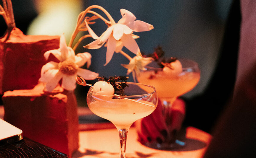 Custom cocktails on a table with a small floral installation.